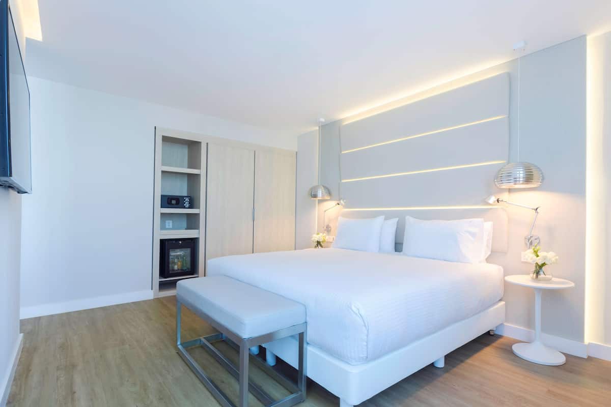 Un dormitorio moderno con una cama grande, mesitas de noche, un banco y estanterías empotradas.