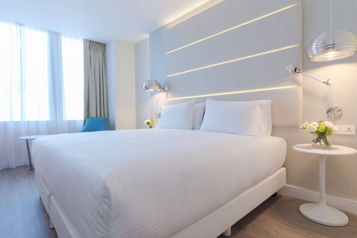 Una habitación de hotel moderna con una cama grande, mesitas de noche y una lámpara fijada a la pared.