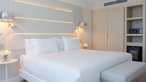 A modern bedroom with a large bed, bedside lamps, a small table with flowers, and built-in storage. - NH Monterrey La Fe (San Nicolas de los Garza)