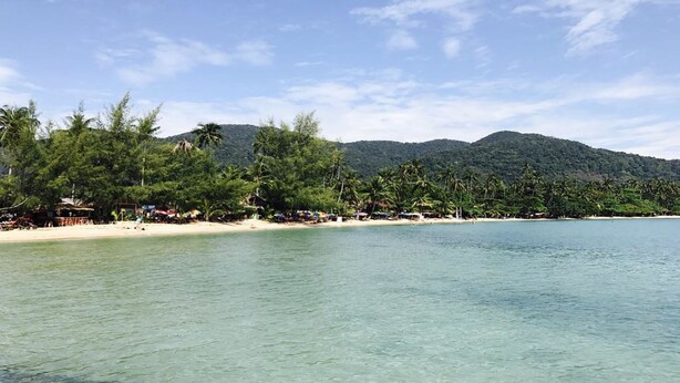 A beach with clear turquoise water, palm trees, and a mountainous backdrop. - Yuyu Golden Beach (Ko Chang)