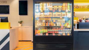 Un moderno vestíbulo de hotel con un dispensador de bebidas central, una recepción y un televisor montado en la pared.