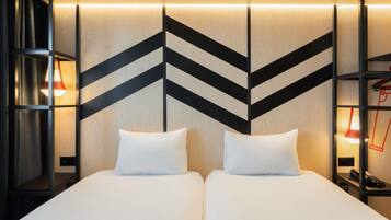 Habitación de hotel con dos camas, un diseño geométrico moderno en la pared y una mesita de noche con lámpara.