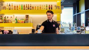 Zona de bar con mostrador, una máquina de café y una variedad de botellas en estanterías.