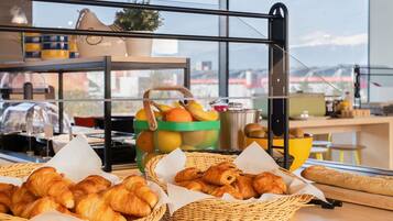 A breakfast buffet with croissants, fruits, and a coffee machine.