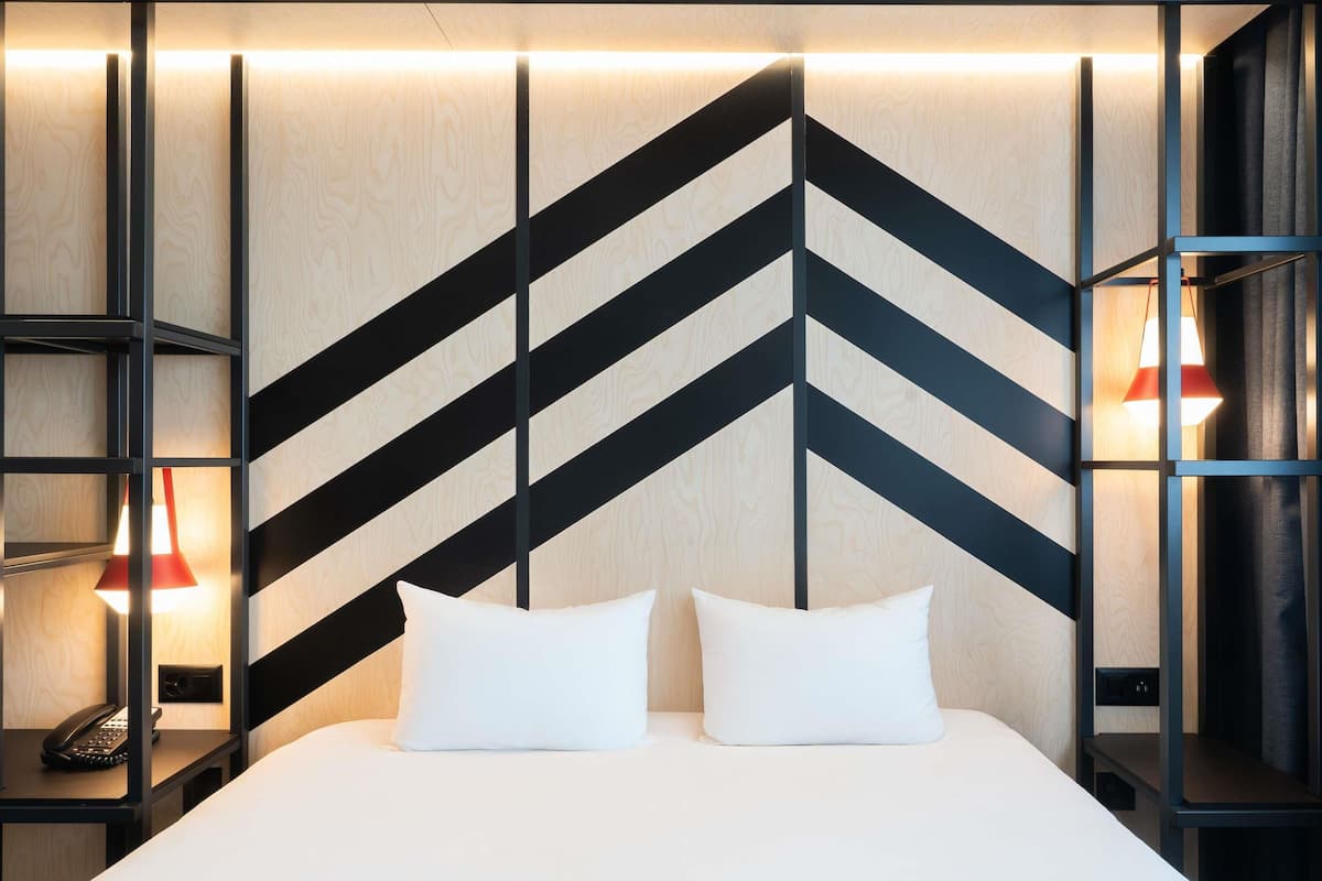 A modern hotel room with a large bed, two bedside tables, and a geometric patterned wall.