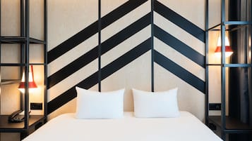 Une chambre d’hôtel moderne avec un grand lit, deux tables de chevet et un mur orné d’un motif géométrique.