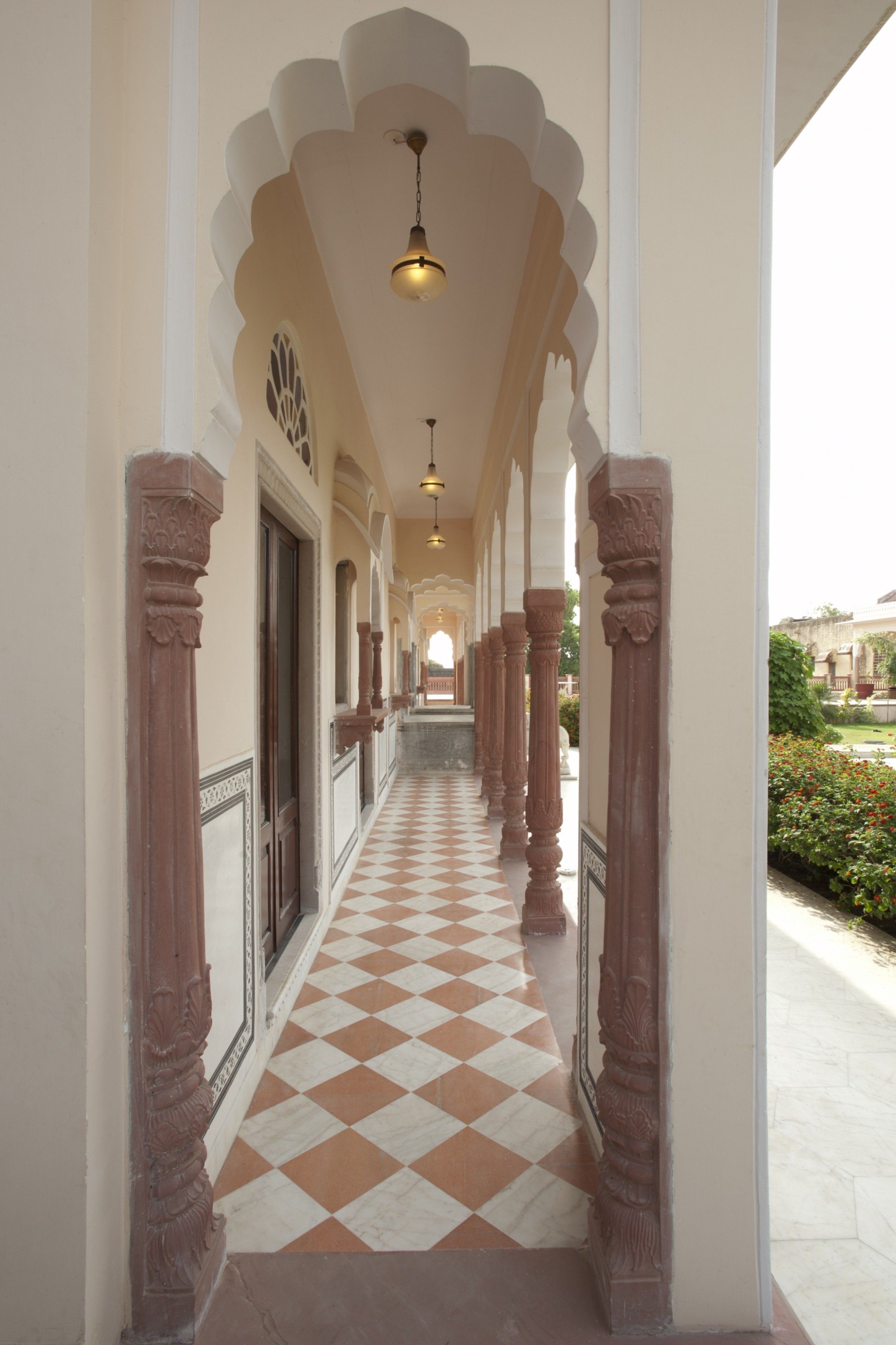 Un pasillo con suelo a cuadros, columnas ornamentadas y una serie de arcos.