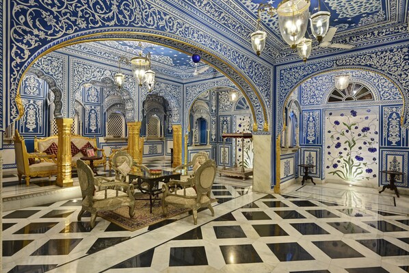 Una habitación lujosa con paredes de azulejos blancos y azules muy decoradas, piso a cuadros y una araña.