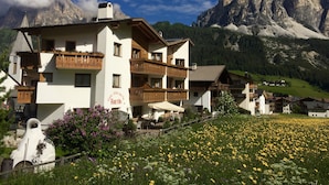 A traditional Alpine-style building with multiple balconies, a café named "Raiffei," and a mountainous backdrop. - Garni Raetia (Corvara in Badia)