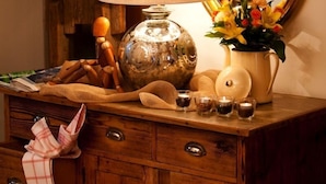 A wooden dresser with a mirror, a lamp, a vase with flowers, and a small jar. - Garni Raetia (Corvara in Badia)