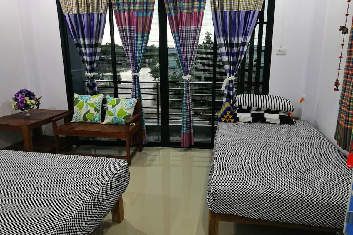 A room with two beds, a wooden chair, a small table with a vase of flowers, and a balcony with colorful curtains.