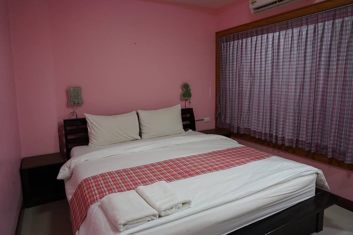 A bedroom with a bed, a nightstand, a wall-mounted air conditioner, and a window with a checkered curtain.
