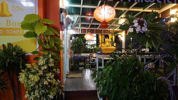 Entrada de un hotel con una escalera que lleva a una zona de recepción, rodeada de plantas en macetas y un letrero que dice "The Boss Tower".