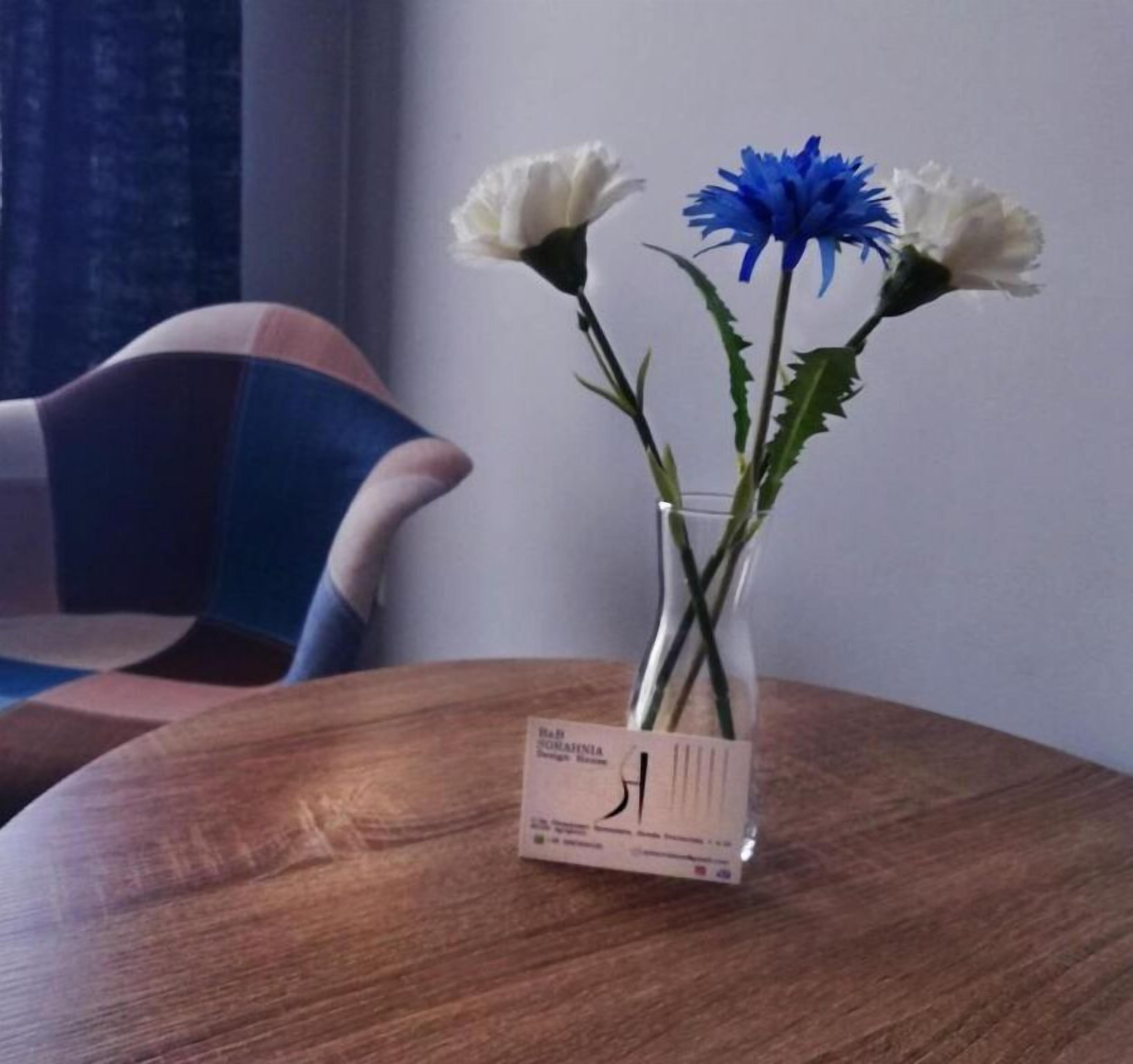 Une table en bois sur laquelle est posé un vase en verre transparent contenant des fleurs blanches et bleues.