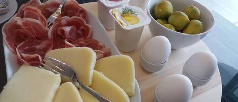 A breakfast tray with prosciutto, cheese, eggs, yogurt with fruit, and green apples.