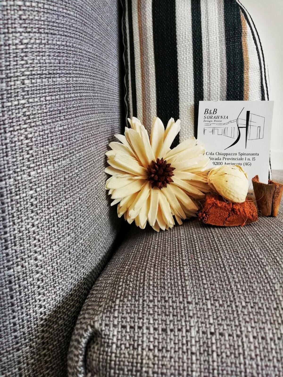 Un canapé gris à la texture particulière, agrémenté d’une fleur décorative et sur lequel est posée une carte de visite.
