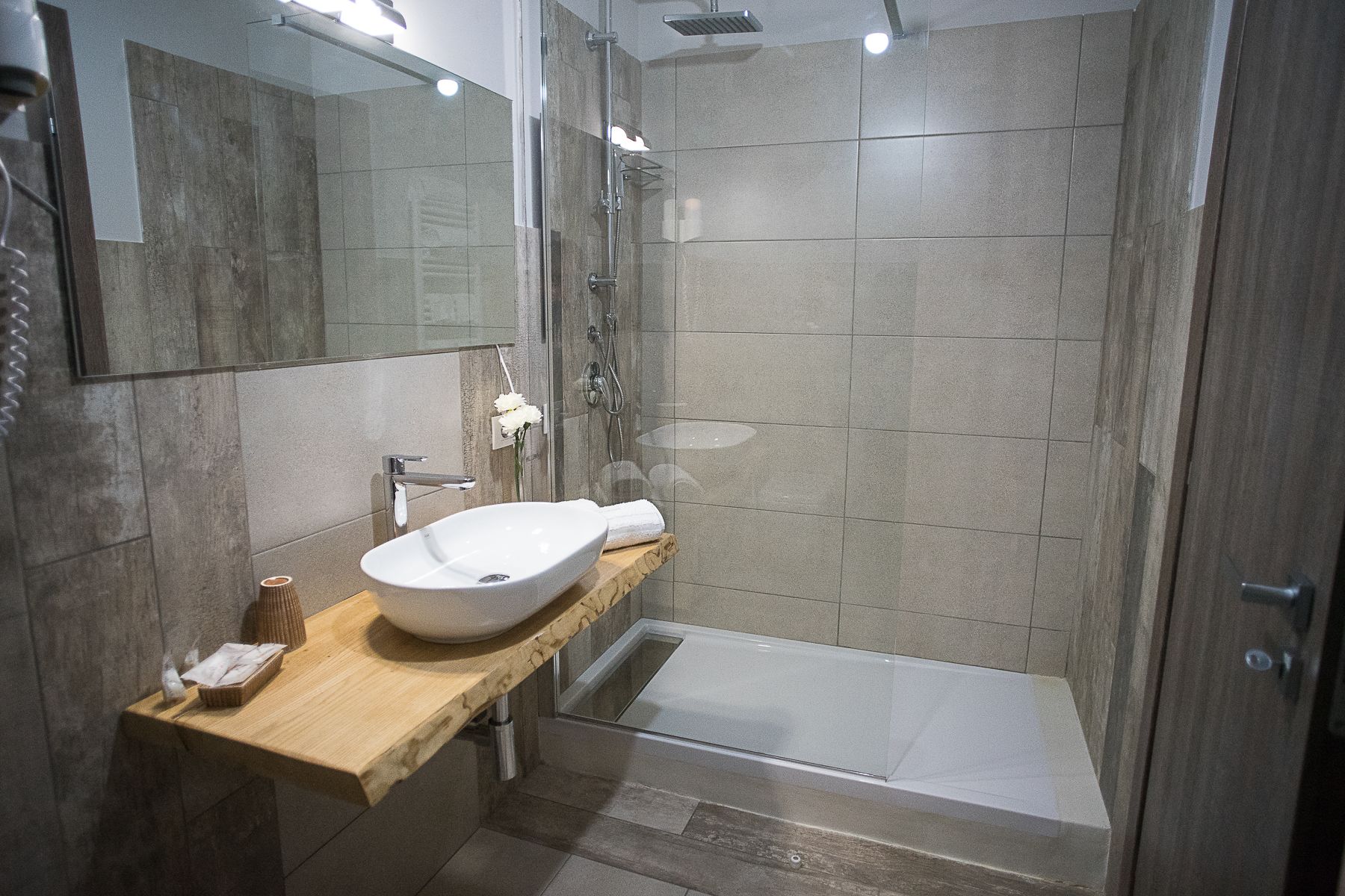 Een moderne badkamer met een vrijstaand badkamermeubel, een douchecabine met glazen wanden en een houten wastafelmeubel.