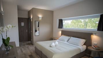 A hotel room with a bed, a bedside table with a book, a window with curtains, and a mirror on the wall.