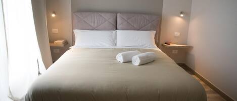 A neatly made bed with a headboard, two bedside tables, and a pair of rolled towels on the bed.