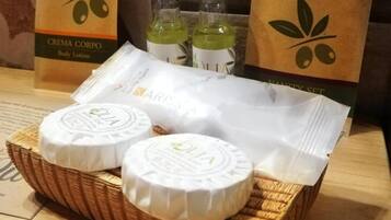 Una cesta de mimbre que contiene dos recipientes redondos etiquetados con “OLIA” y una bolsa de papel blanca con la marca “ARISSA”.