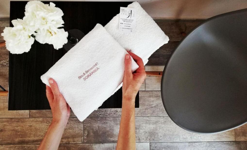 A person holding a white towel with "SOMBRANA" printed on it, a black table with a white flower, and a black bowl.