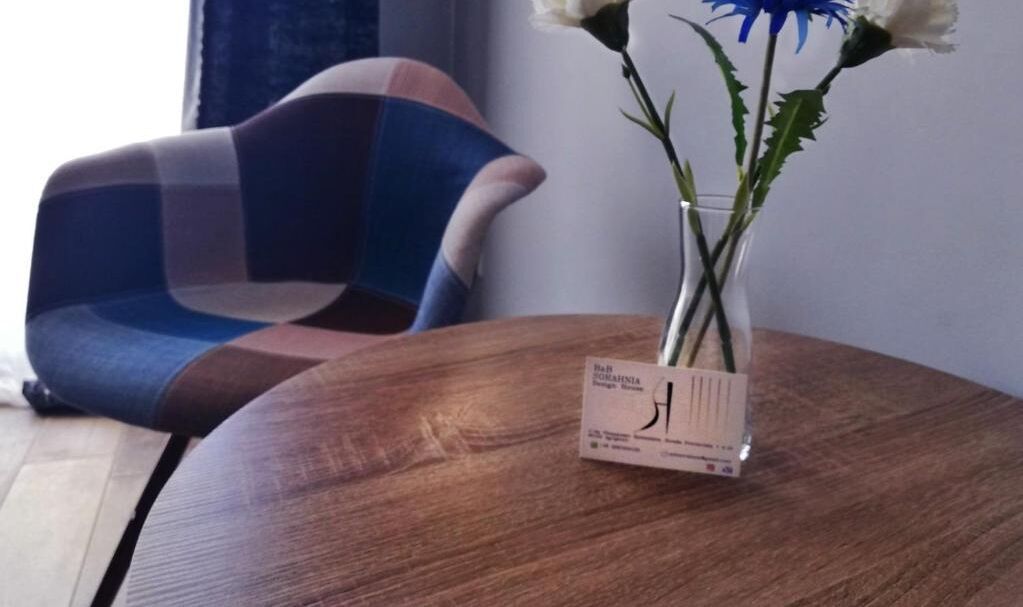 Una mesa de madera con un jarrón con flores blancas y azules, y una tarjeta de identificación encima.