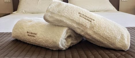 A bed with white linens and two rolled towels on a brown quilted bedspread.