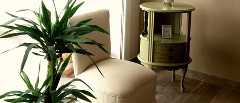 A corner room with a potted plant, a chair, a small table with a vase of flowers, and a glass table.