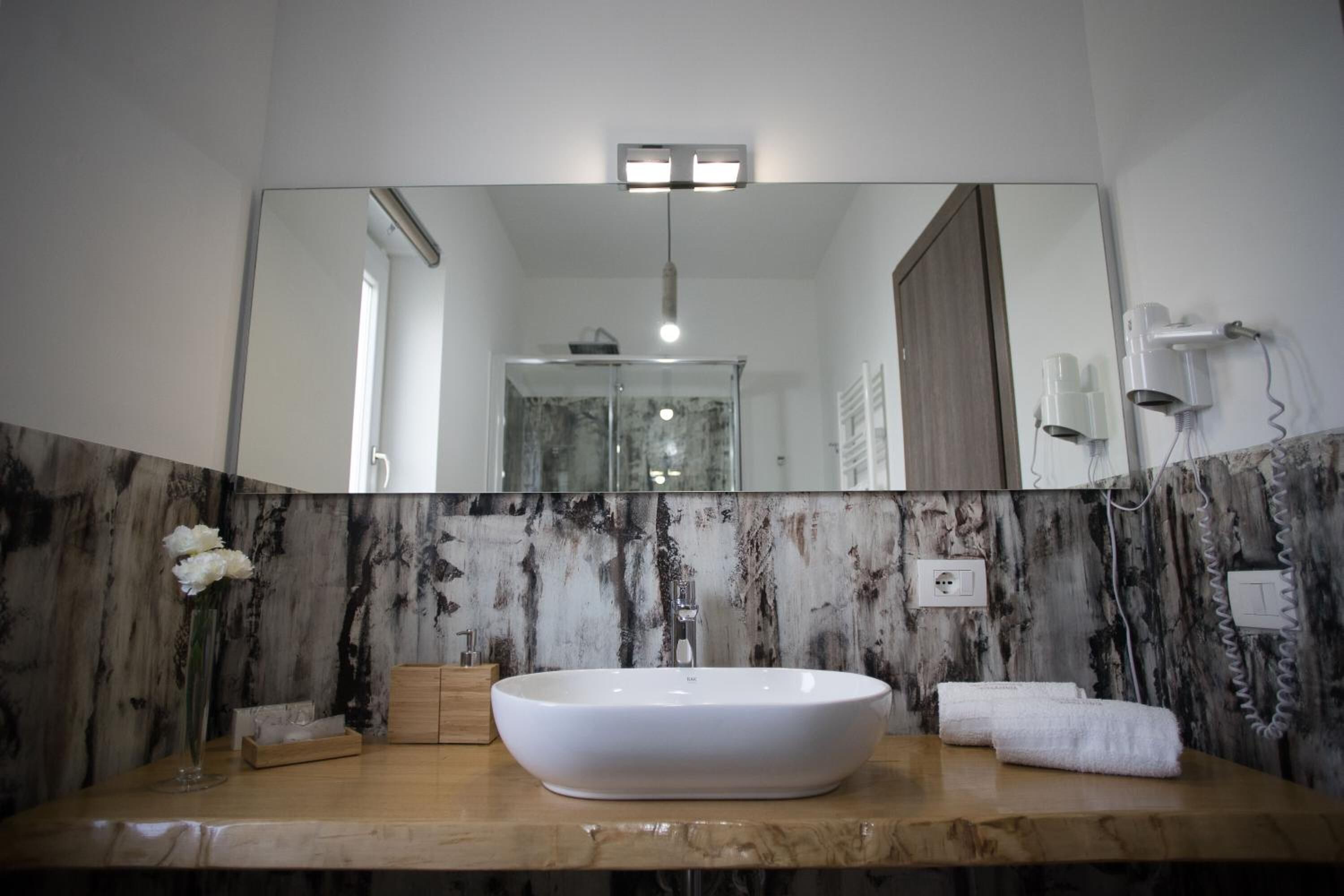 A bathroom with a large mirror, a white sink, a marble wall, a wooden vanity, and a towel rack.