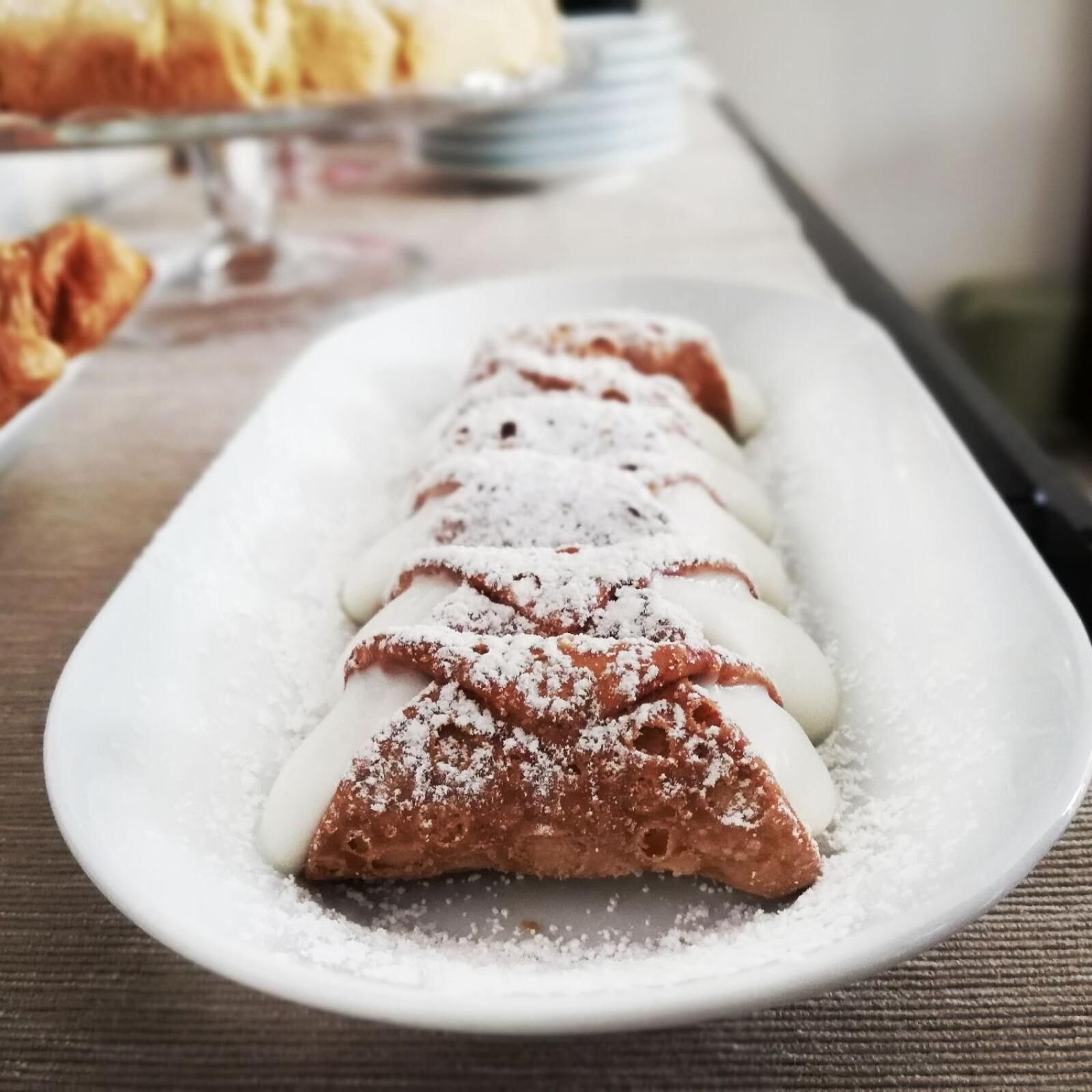Un postre sobre un plato blanco, posiblemente un pastel o crepe, espolvoreado con azúcar glas.