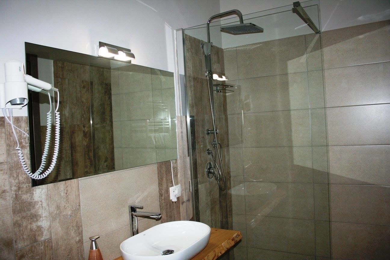A modern bathroom with a glass-enclosed shower, a white sink, and a hairdryer mounted on the wall.