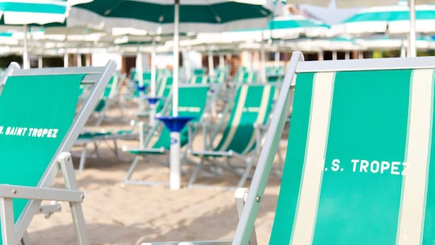 Rows of beach chairs and umbrellas with "S. TROPEZ" branding, arranged on a sandy beach. - Hotel Saint Tropez (Pineto)