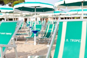 Rows of beach chairs and umbrellas with "S. TROPEZ" branding, arranged on a sandy beach. - Hotel Saint Tropez (Pineto)