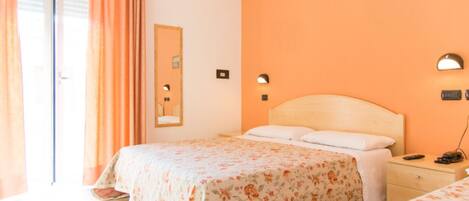 A hotel room with two beds, a large window with curtains, a wall-mounted mirror, and a bedside table with a lamp.