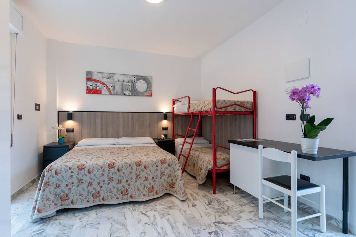 A bedroom with two beds, a desk, a chair, a potted plant, and a painting on the wall.