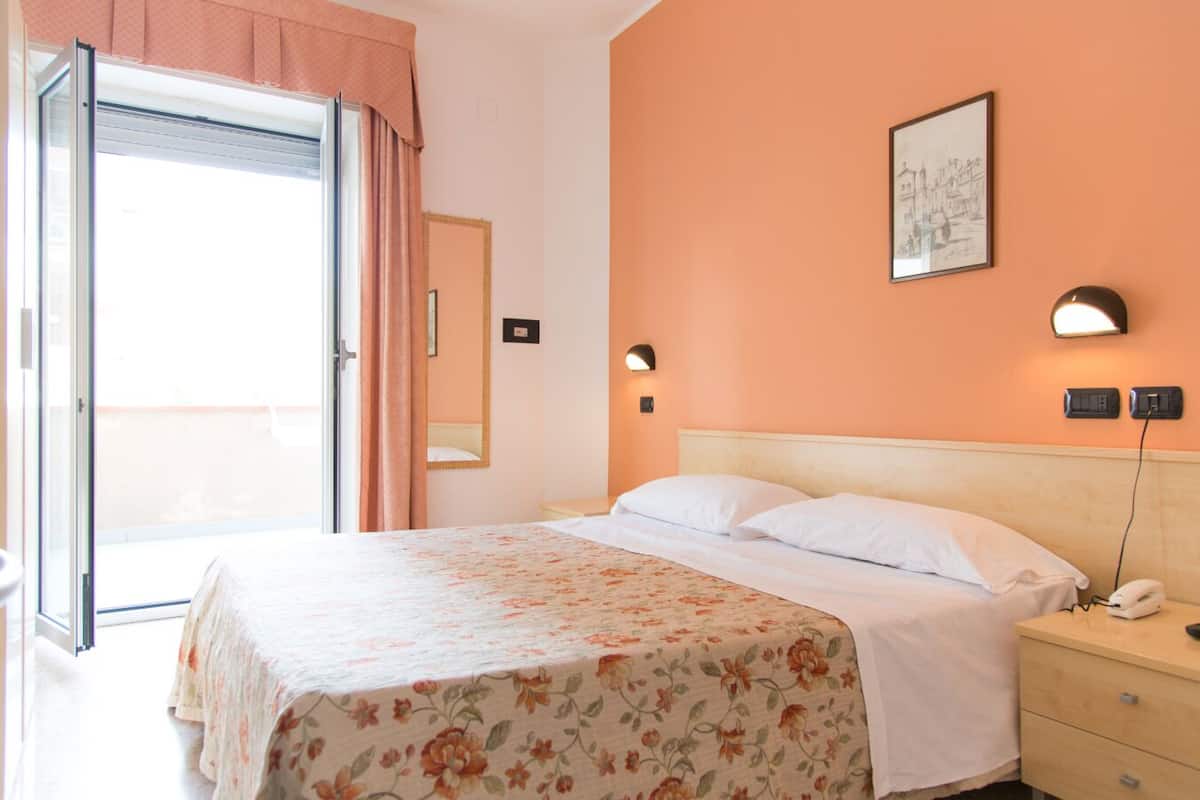 A hotel room with a bed, a nightstand, a mirror, and a window with curtains.