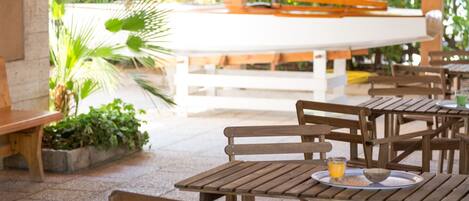 Un espace extérieur aménagé en terrasse, avec des tables et des bancs en bois, entouré de verdure.