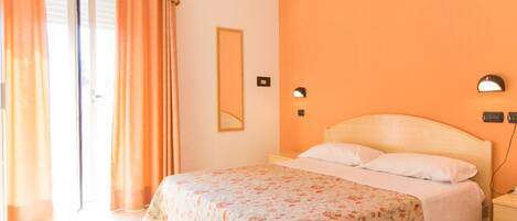 A bedroom with a bed, a nightstand, a mirror, and a sliding door.