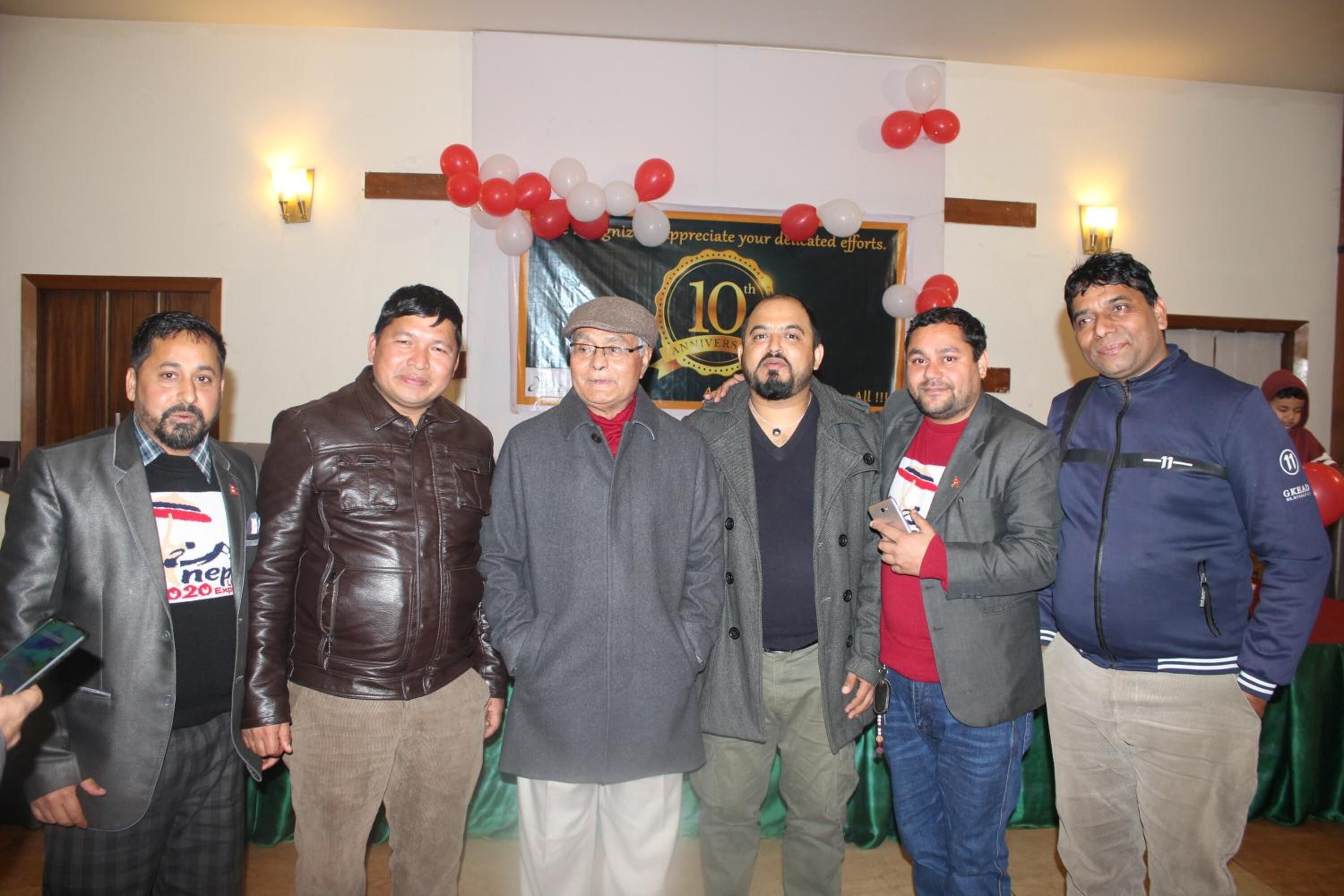 Un grupo de personas de pie en una habitación con un cartel que indica una celebración por el décimo aniversario.