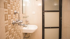 A bathroom with a tiled wall, a sink, and a shower area. - Mirage Inn (Lumbini)