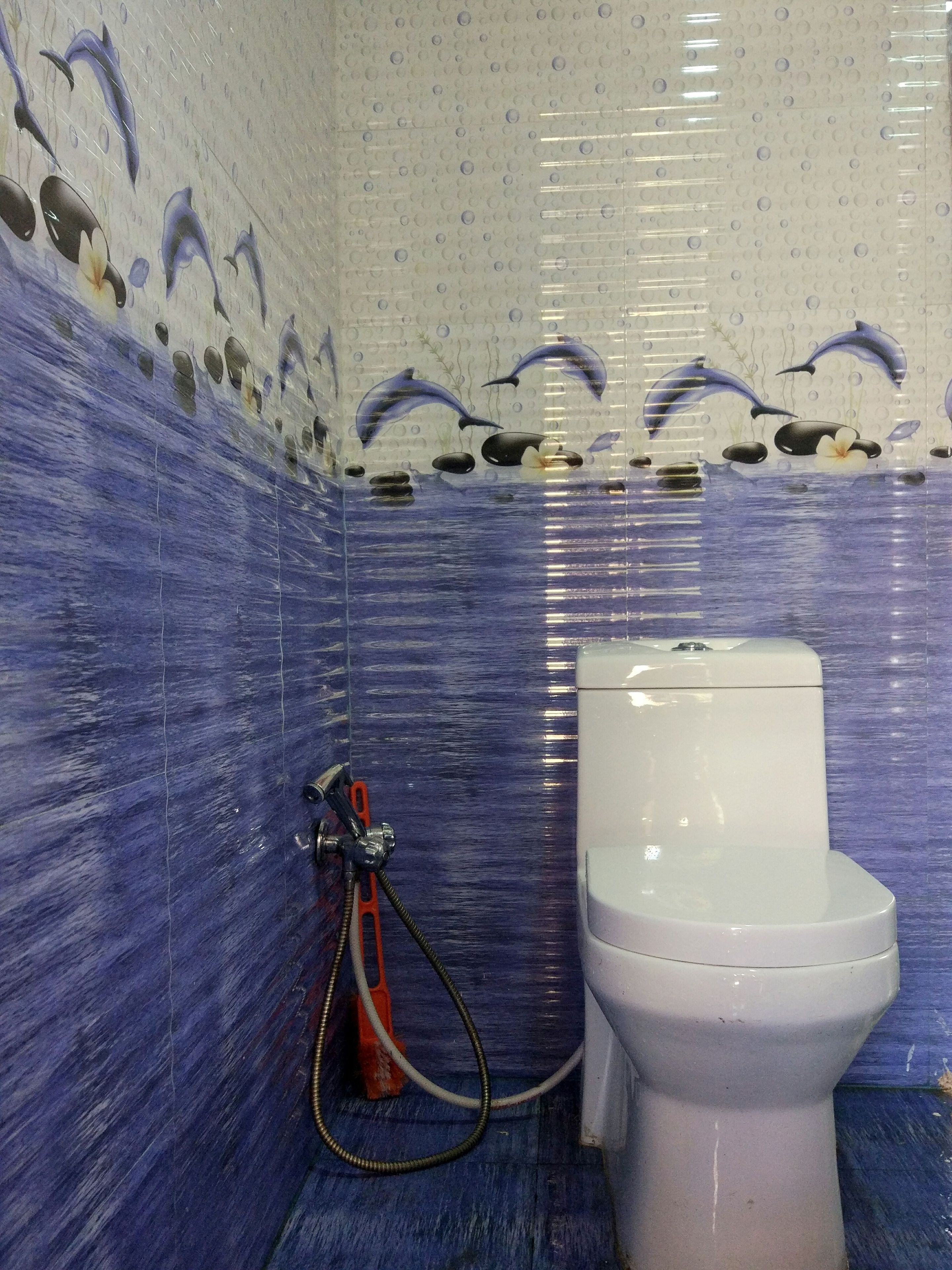 A bathroom with blue tiled walls, a white toilet, and a shower hose.