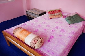 A bed with a floral patterned bedspread and multiple pillows, a wooden headboard, and a small bedside table with a patterned cloth. - Everest Home Stay Apartment (Imadol)