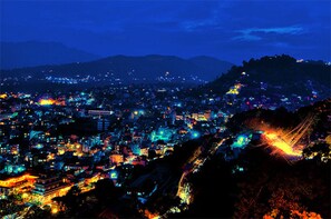Un paisaje urbano nocturno con edificios iluminados y montañas al fondo.