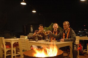 A group of people sitting around a table with a fire in the center, surrounded by chairs and tables. - Everest Home Stay Apartment (Imadol)