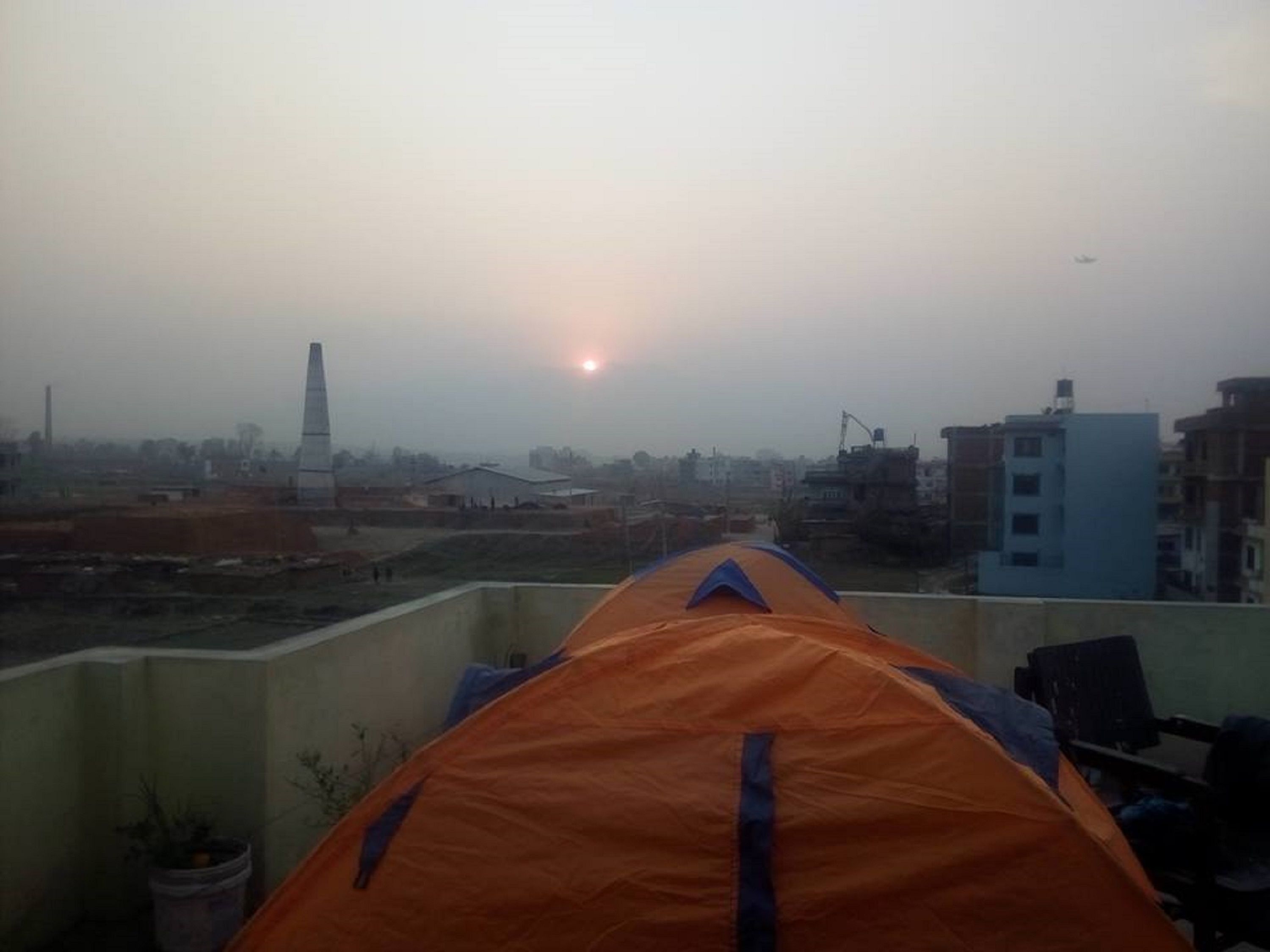 A tent on a rooftop with a view of a cityscape, including buildings and a distant tower.