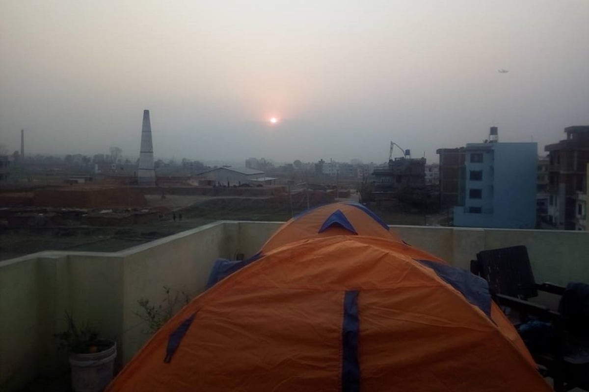 A tent on a rooftop with a view of a cityscape, including buildings and a distant tower.