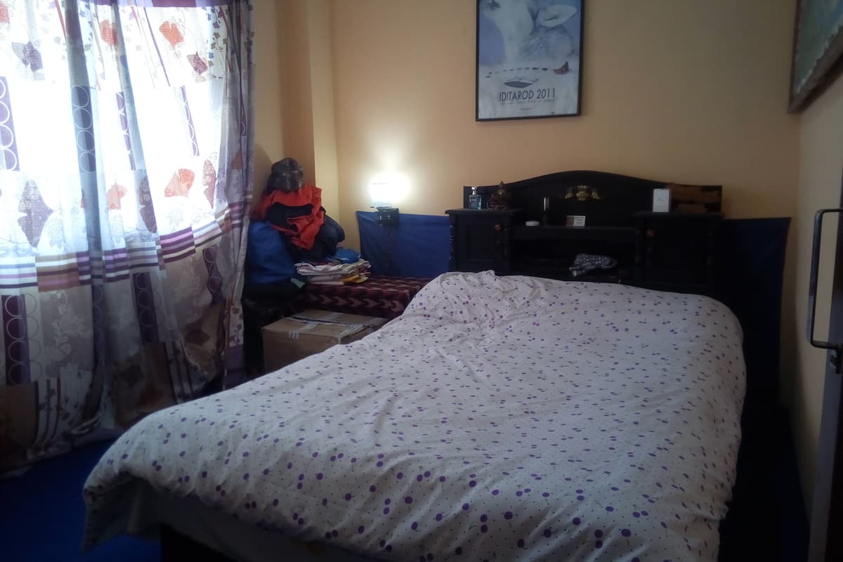 A bedroom with a bed, a desk, and a chair. There is a poster on the wall and a window with curtains.