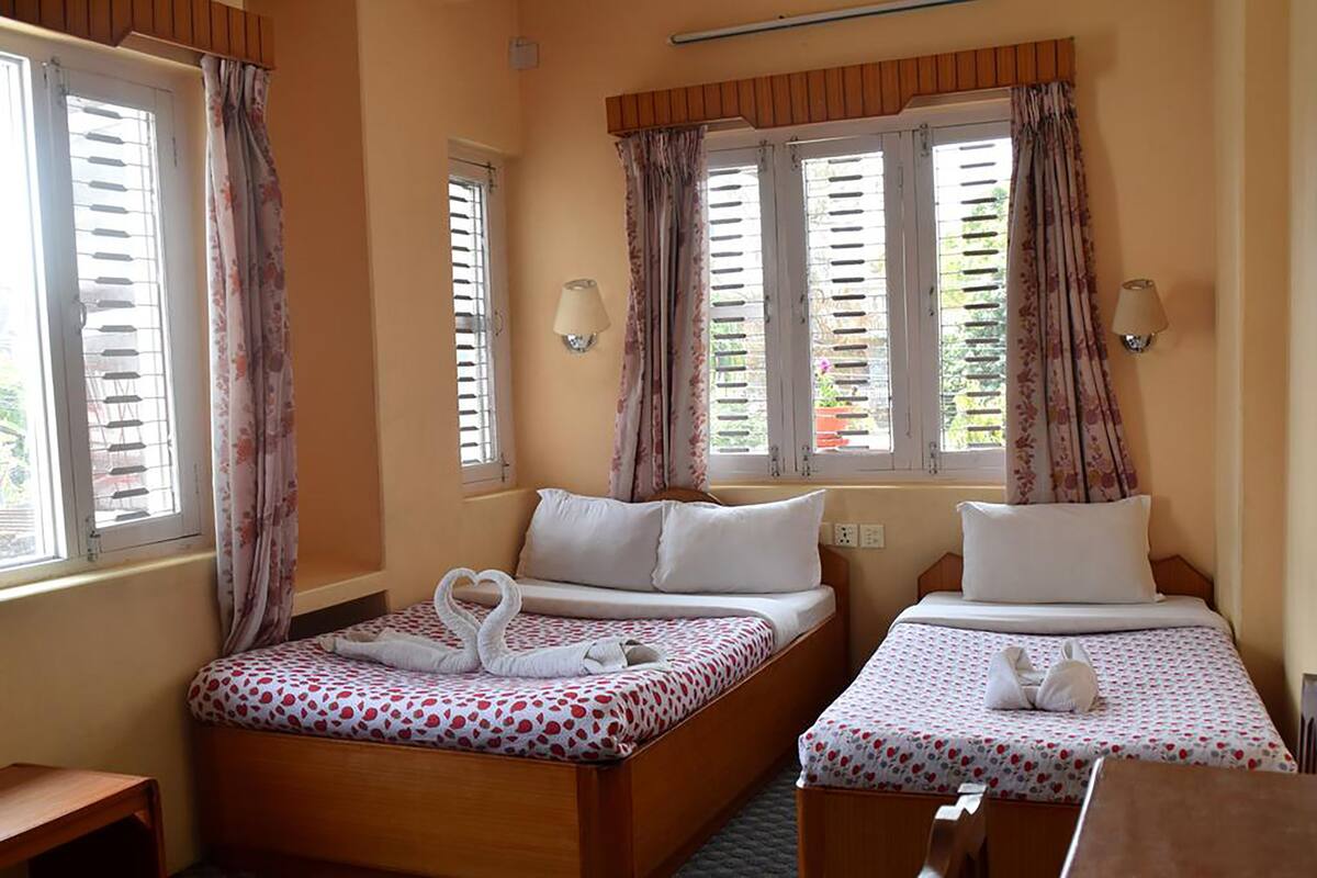 A hotel room with two beds, each with a floral-patterned bedspread and a pair of towels arranged in a heart shape.