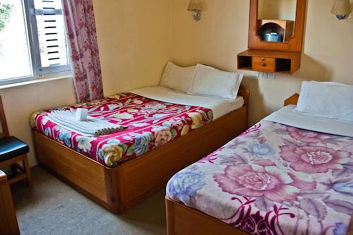 A room with two single beds, a wooden nightstand, a small table, and a window with curtains.
