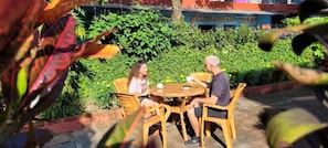 An outdoor seating area with a round table and chairs, surrounded by greenery.